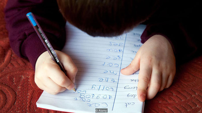 یک بچه دراز کش با دفتر و قلم به دست درحال نوشتن حروف انگیلسی